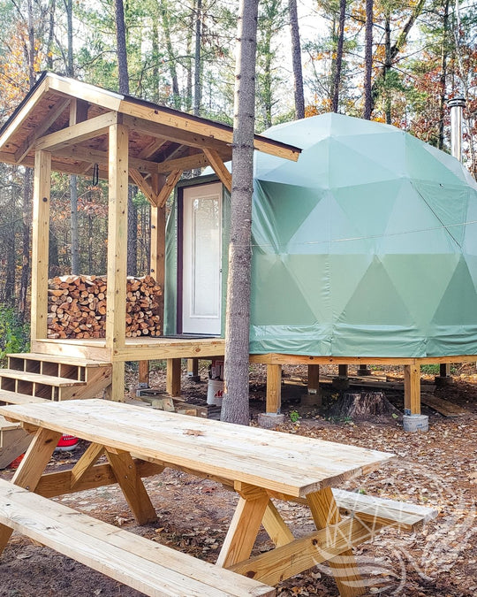 Geodesic dome structure with wooden deck and picnic table in a forest setting